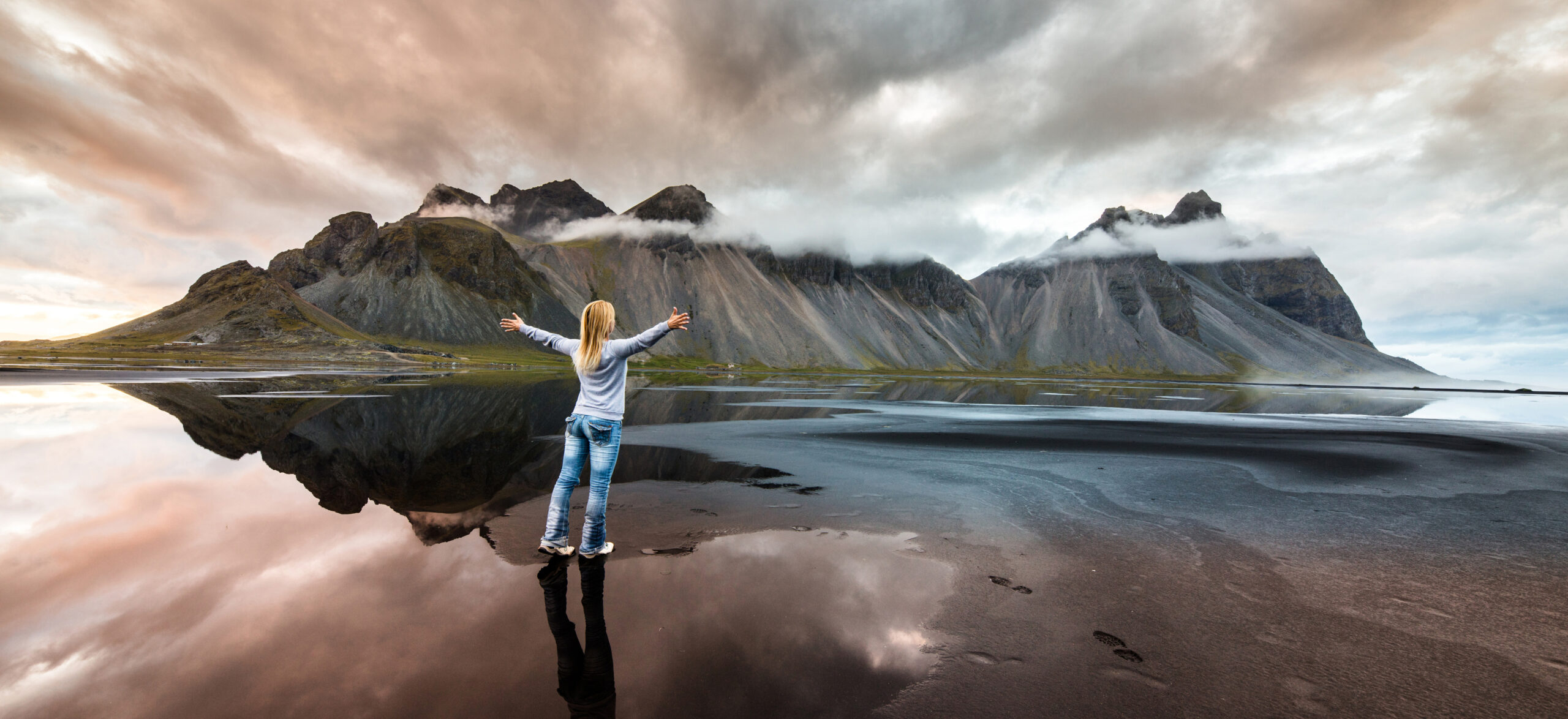 Back view of a woman feeling free at Vestrahorn mountain at Stokksness peninsula, Iceland.